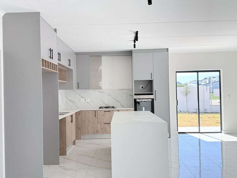 Modern open-plan kitchen featuring a central island, built-in oven, gas hob, and sleek cabinetry, leading directly to an outdoor patio area.