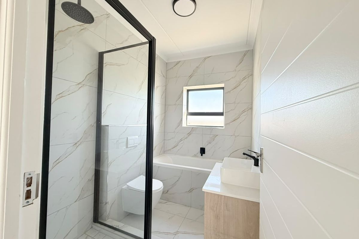 Modern bathroom featuring a walk-in shower with black frame, built-in bathtub, wall-hung toilet, and a vanity with a vessel sink, finished with marble-look tiles.