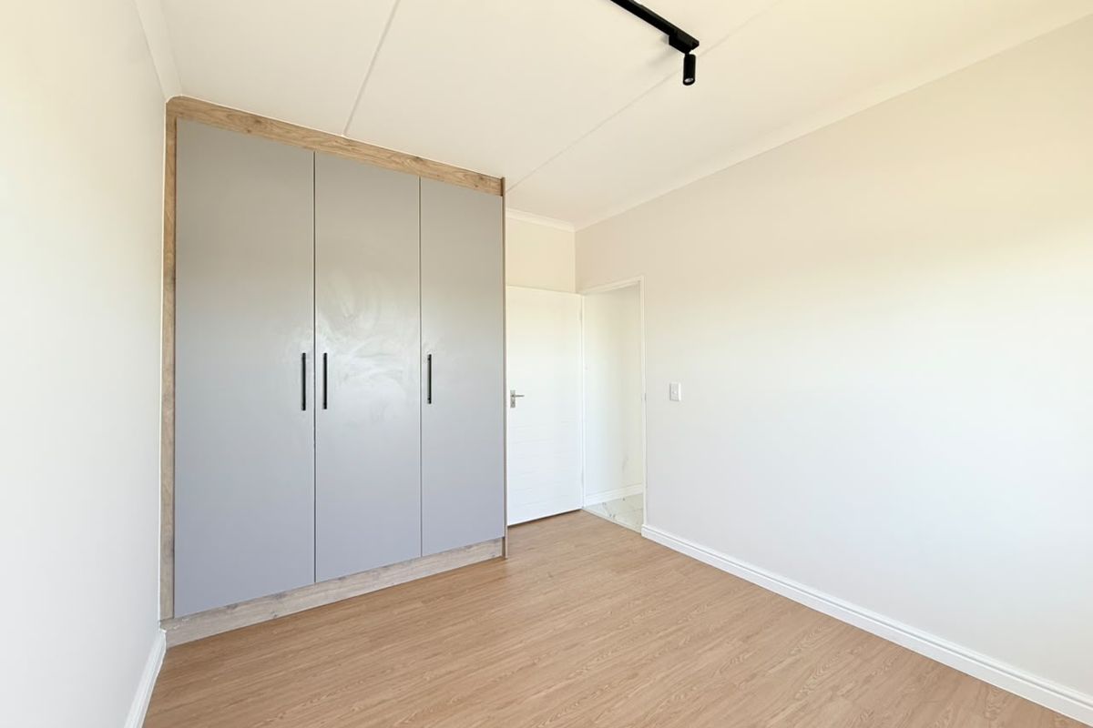 A bright, empty bedroom featuring modern laminate flooring, a built-in wardrobe with grey doors, and contemporary track lighting.