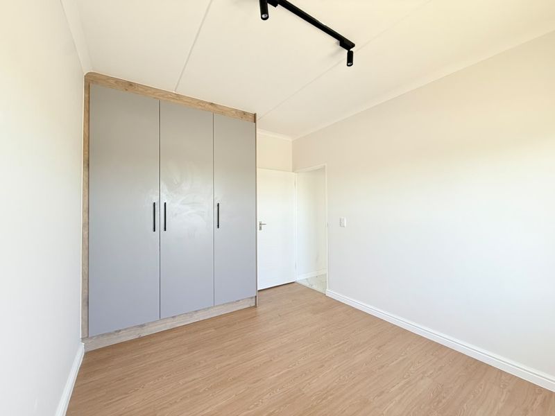 A bright, empty bedroom featuring modern laminate flooring, a built-in wardrobe with grey doors, and contemporary track lighting.