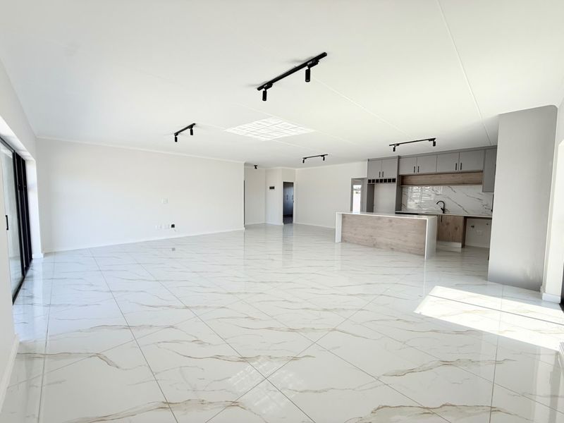 Spacious open-plan living and kitchen area featuring modern marble-look floor tiles, sleek cabinetry, and contemporary track lighting in a bright, neutral setting.