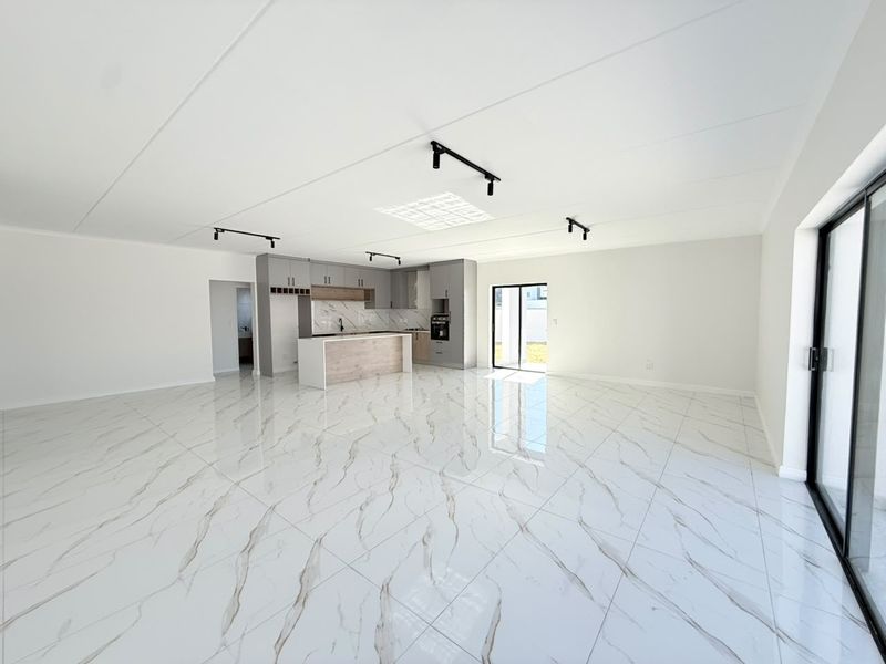 Spacious open-plan living area featuring high-gloss marble-look floor tiles, modern kitchen cabinetry with an island, and large sliding doors leading to the exterior.