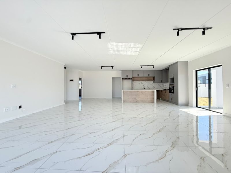 Spacious open-plan living and kitchen area featuring modern marble-look floor tiles, sleek cabinetry, and direct access to the outdoor space.