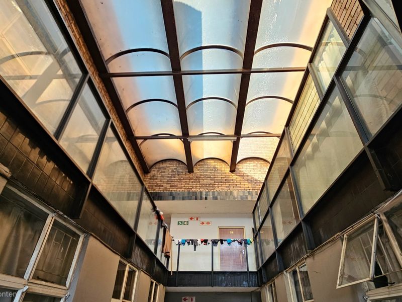 A commercial hallway featuring a large arched skylight, exposed brick walls, and metal-framed windows, providing natural light to the corridor.