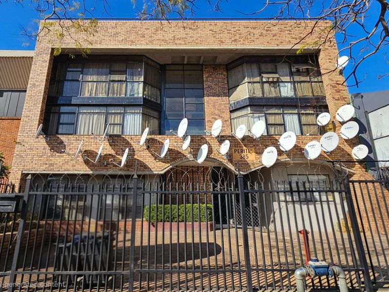 Front elevation of a commercial brick building featuring extensive security fencing, razor wire, and numerous satellite dish installations on the facade.