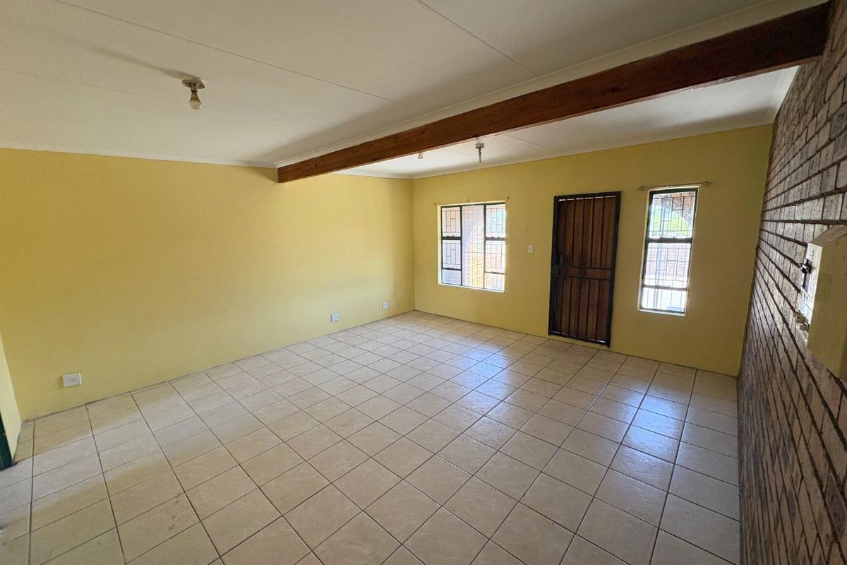 Spacious, empty living area featuring ceramic floor tiles, an exposed timber ceiling beam, and a characterful exposed brick feature wall.