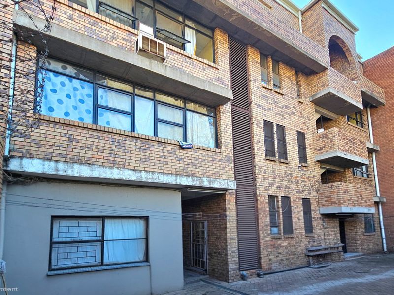 Rear view of a multi-story commercial brick building featuring concrete balconies, paved courtyard area, and metal-framed windows.