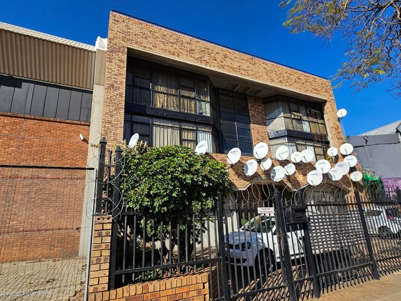 Front exterior view of a commercial brick building featuring metal security fencing, razor wire, and multiple satellite dishes mounted on the facade.