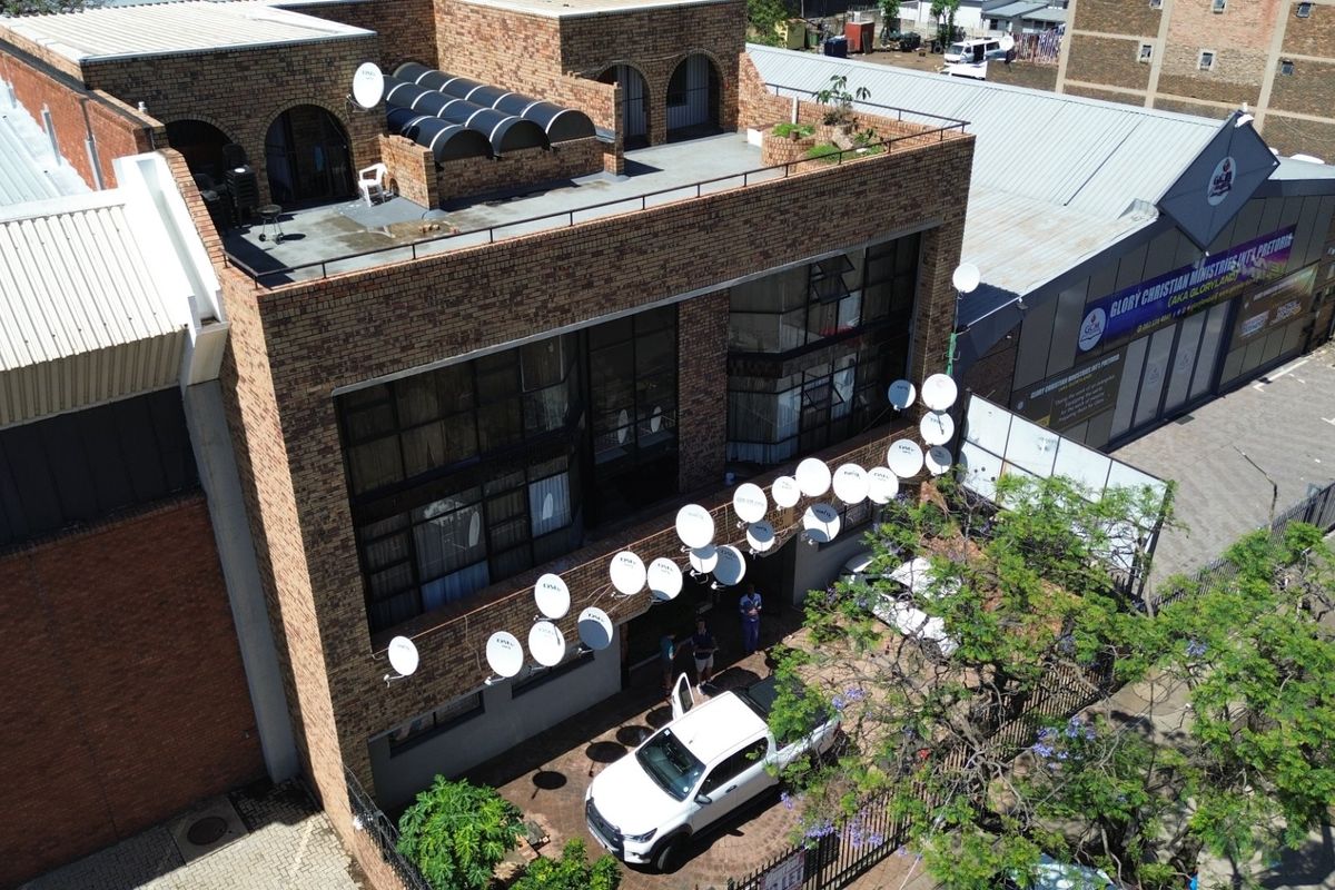Aerial view of a multi-story commercial brick building featuring a flat roof terrace and numerous satellite dishes mounted on the exterior facade.