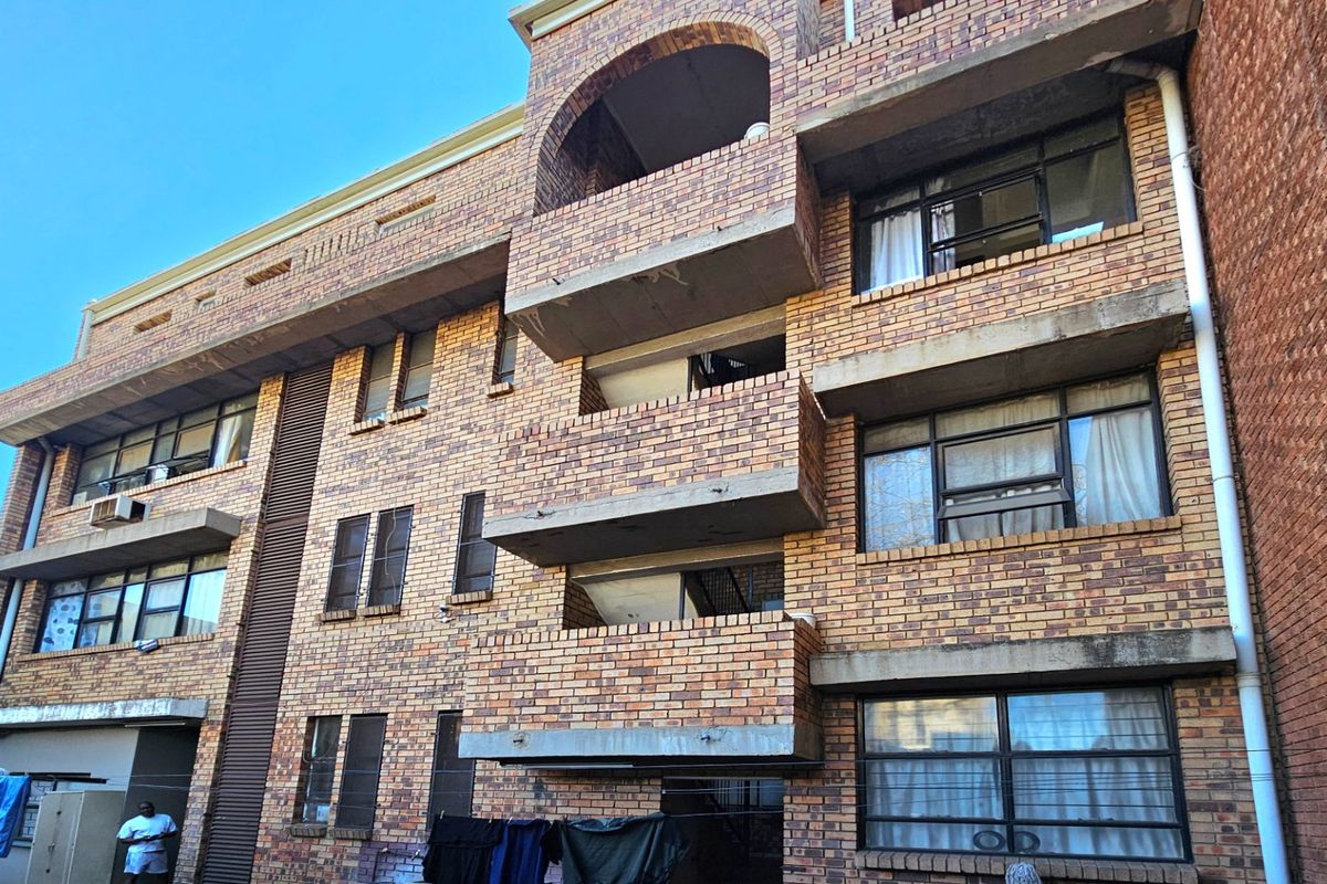 Rear elevation of a multi-story commercial or residential building featuring face brick construction, integrated concrete balconies, and steel-framed windows.