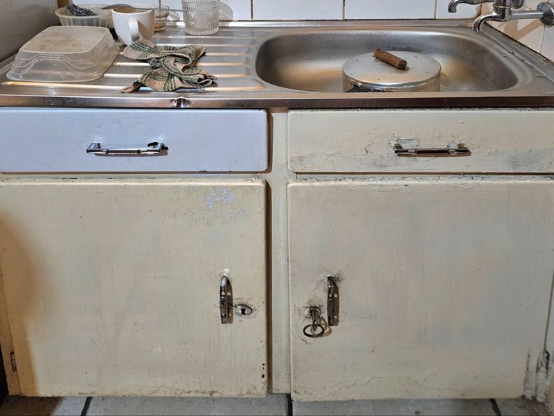 A dated kitchen sink area featuring a stainless steel basin and worn, painted cabinetry in need of refurbishment.