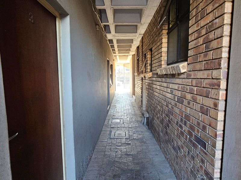 An exterior narrow walkway featuring exposed brick walls, paved flooring, and a waffle slab ceiling structure.