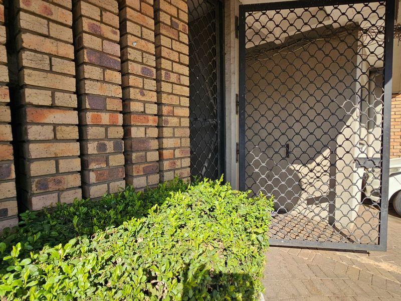 Front entrance area featuring a brick facade, security gate, and paved driveway access.