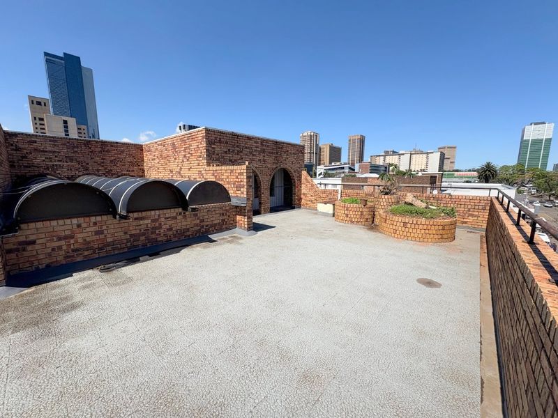 Spacious rooftop terrace featuring brick parapet walls, built-in planters, and curved metal awnings, offering an open-air space with city skyline views.
