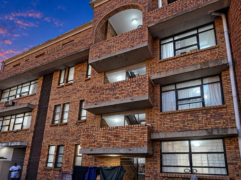 Rear elevation of a multi-story commercial or residential building featuring face brick construction, concrete balconies, and aluminium-framed windows.