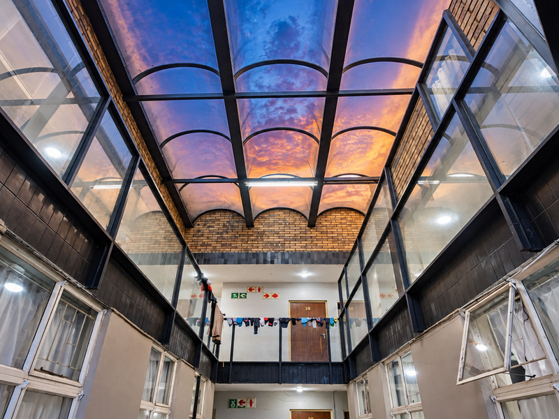An interior atrium-style hallway featuring a large glass skylight, exposed brick walls, and metal structural framing, providing access to multiple units.