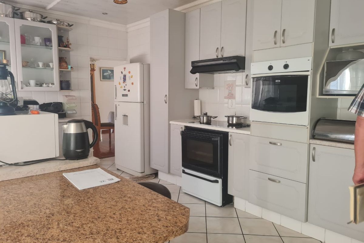 A functional kitchen featuring light grey cabinetry, granite countertops, built-in oven and hob, and tiled flooring throughout.