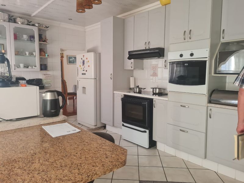 A functional kitchen featuring light grey cabinetry, granite countertops, built-in oven and hob, and tiled flooring throughout.