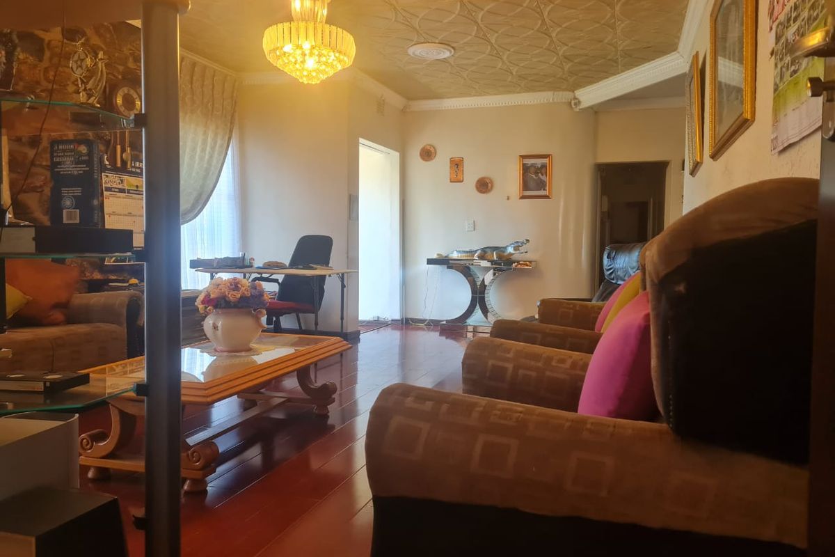 A living room featuring laminate flooring, decorative ceiling tiles, and a central chandelier, offering a traditional aesthetic with potential for modern updates.