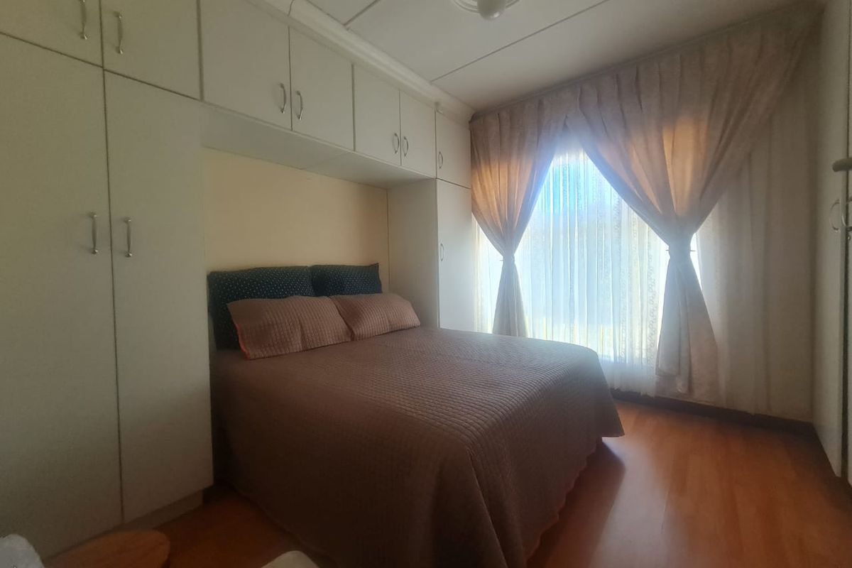 A bedroom featuring built-in cupboards, laminate flooring, and a ceiling rose, offering a functional and well-utilized space.