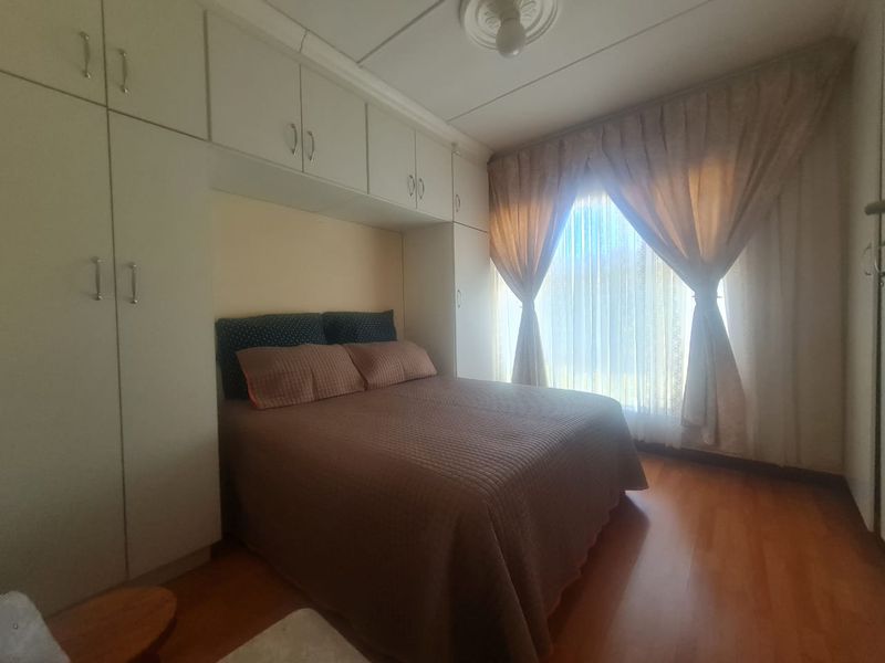 A bedroom featuring built-in cupboards, laminate flooring, and a ceiling rose, offering a functional and well-utilized space.