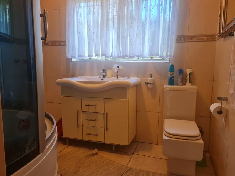A functional bathroom featuring a vanity cabinet with basin, a toilet, and a shower enclosure with tiled walls and flooring.