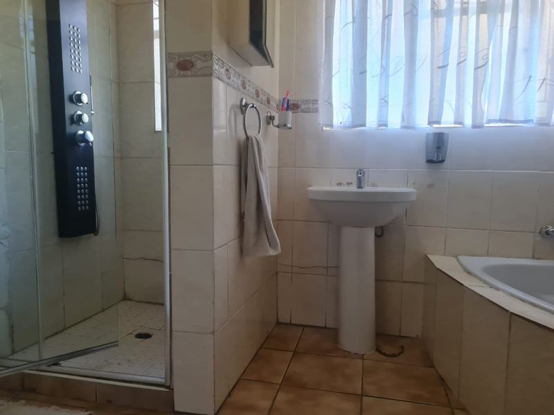 Bathroom featuring a pedestal basin, built-in bathtub, and a shower enclosure with a modern shower panel, requiring cosmetic updates to tiles and finishes.