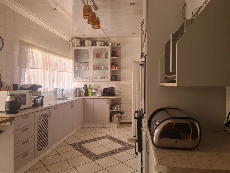 A functional kitchen featuring tiled flooring, ample built-in cabinetry, a double sink, and a tiled splashback with integrated oven and lighting.