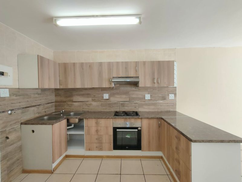 A functional kitchen featuring wood-look cabinetry, stone-effect countertops, built-in oven, gas hob, and tiled backsplash. The space is clean and ready for updates.