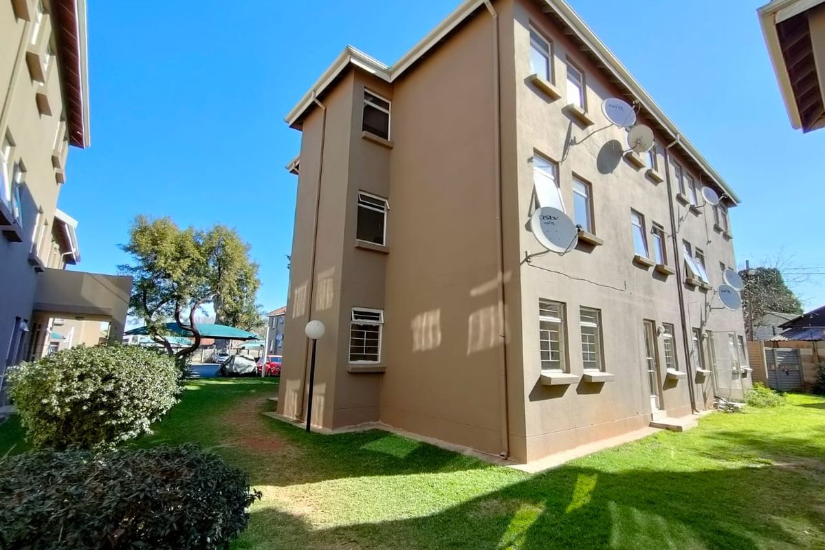 Rear elevation of a multi-story townhouse complex featuring brown painted facade, multiple satellite dishes, and security-fitted windows overlooking a communal garden area.