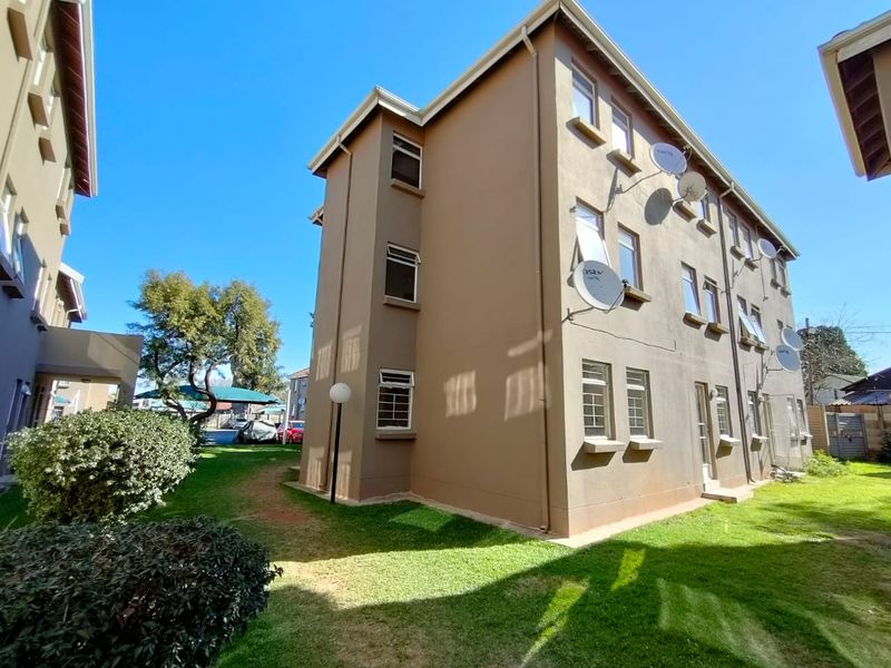 Rear elevation of a multi-story townhouse complex featuring brown painted facade, multiple satellite dishes, and security-fitted windows overlooking a communal garden area.