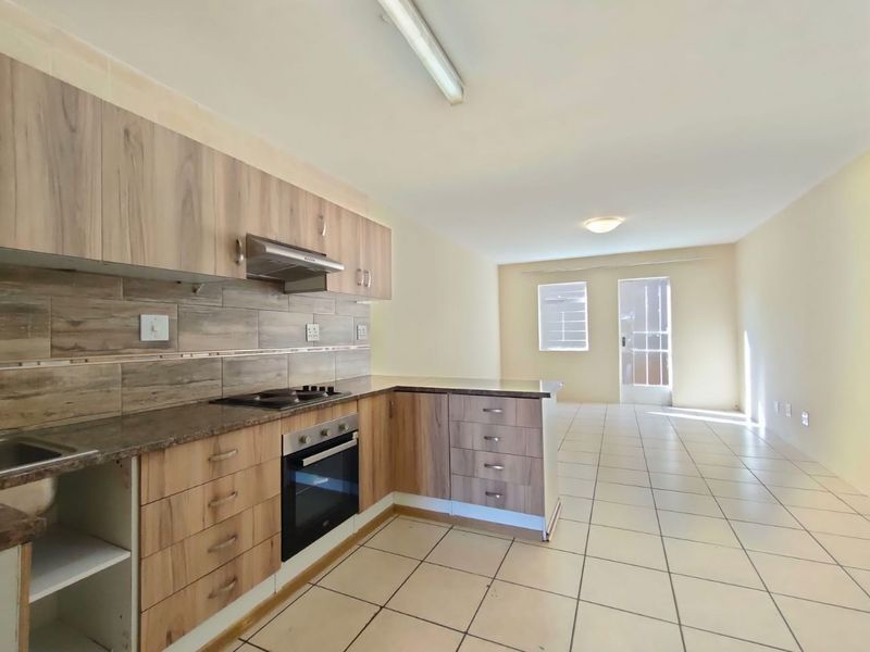 Open-plan kitchen and living area featuring wood-look cabinetry, built-in oven and hob, tiled flooring, and direct access to the exterior.
