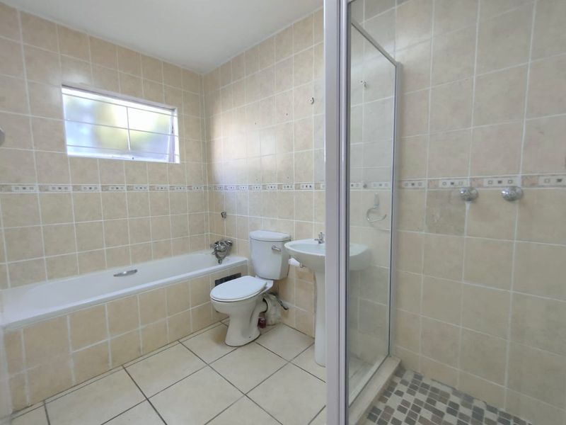 A functional bathroom featuring a bathtub, separate shower enclosure, pedestal basin, and toilet with neutral wall and floor tiling.