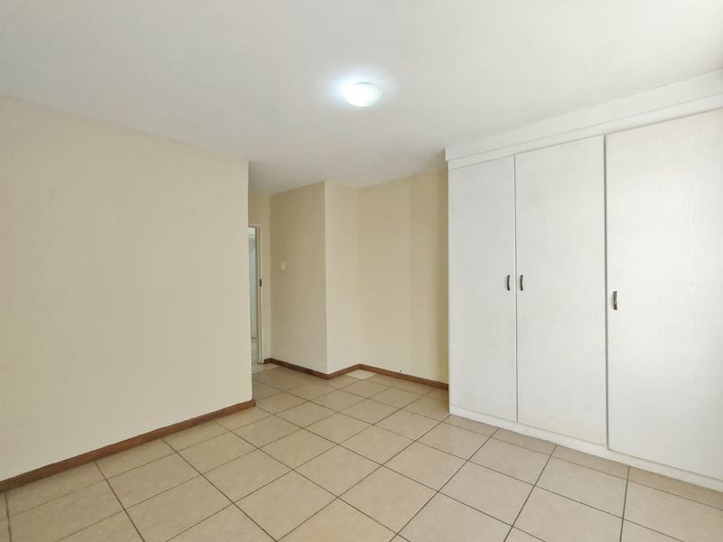 A clean, empty bedroom featuring neutral tiled flooring and a large built-in wardrobe with white cabinetry.