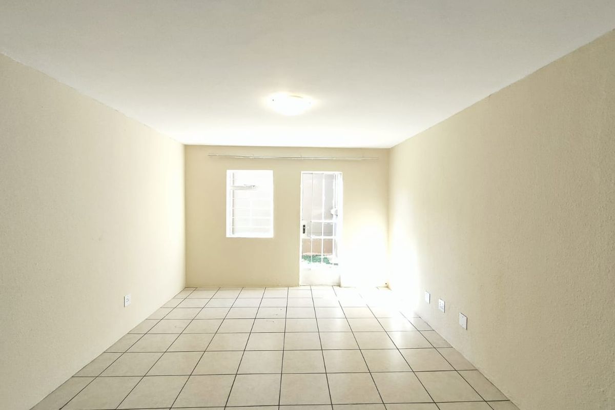 An empty, neutrally painted living area featuring tiled flooring, a ceiling light, and direct access to an outdoor space through a glass panel door.