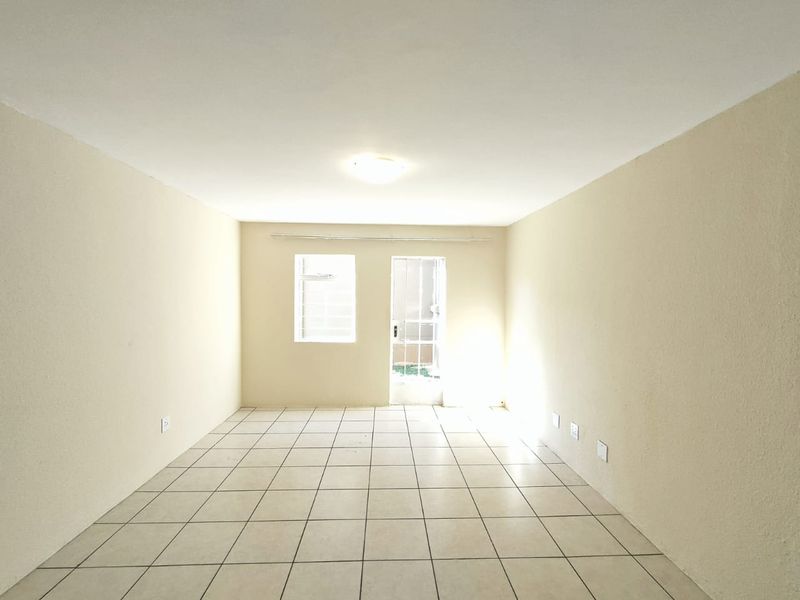 An empty, neutrally painted living area featuring tiled flooring, a ceiling light, and direct access to an outdoor space through a glass panel door.