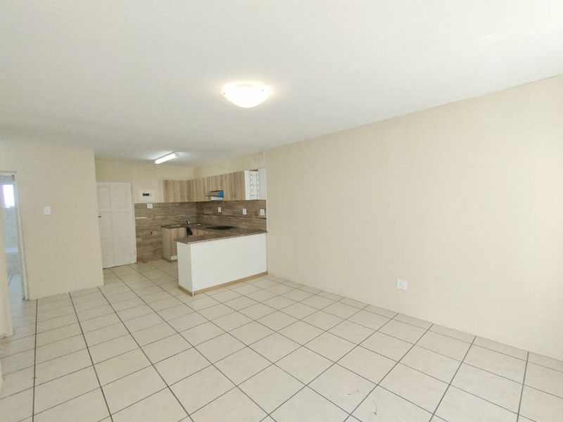 An open-plan living and kitchen area featuring ceramic tile flooring, neutral walls, and functional built-in kitchen cabinetry with a breakfast counter.