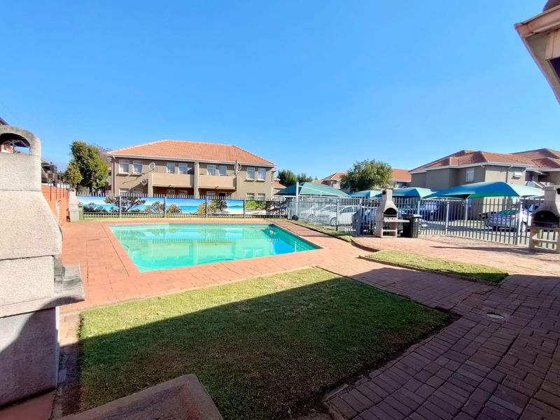 Communal pool area featuring brick paving, built-in braai facilities, and metal perimeter fencing within a townhouse complex.