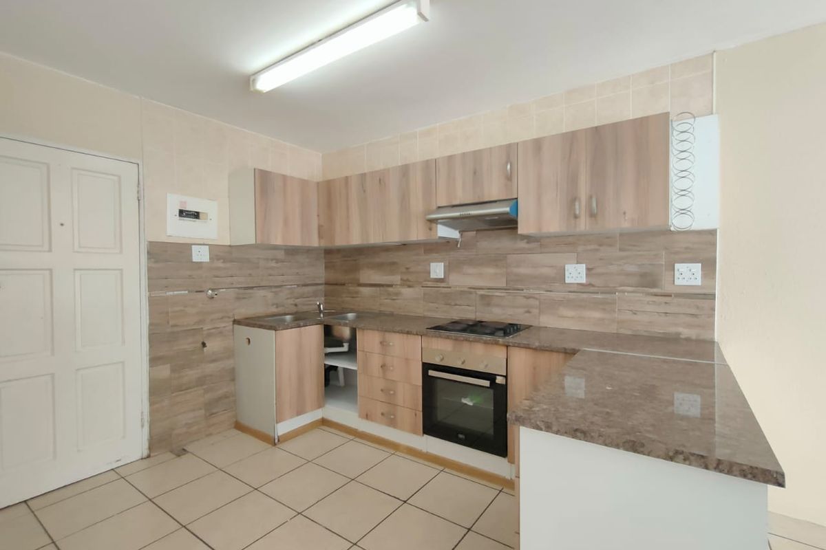 A functional kitchen featuring wood-look cabinetry, built-in oven and hob, tiled backsplash, and tiled flooring. The space is currently vacant and ready for updates.