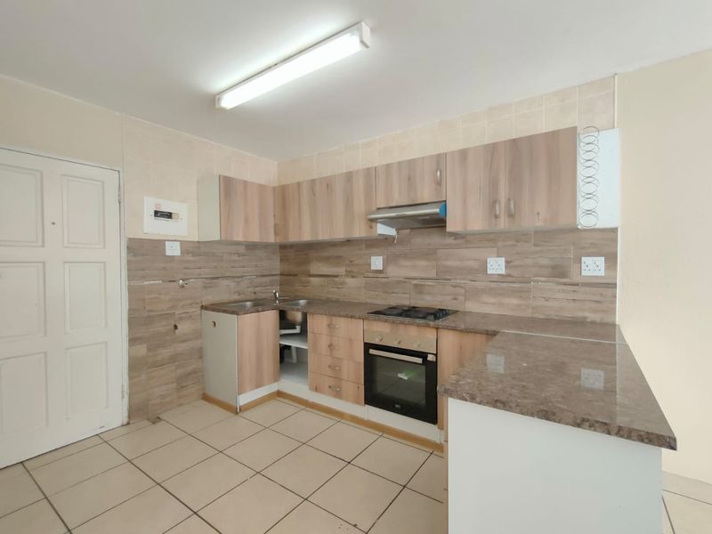 A functional kitchen featuring wood-look cabinetry, built-in oven and hob, tiled backsplash, and tiled flooring. The space is currently vacant and ready for updates.