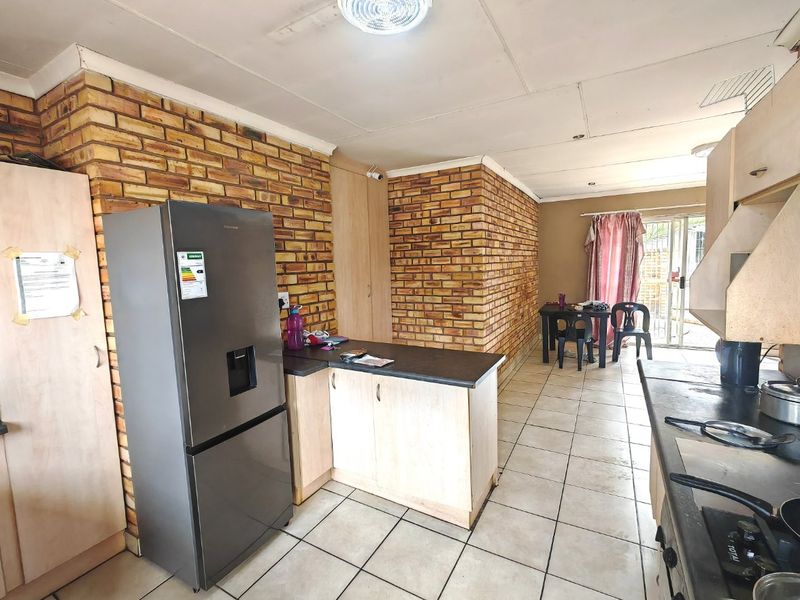 Open plan kitchen and living area featuring exposed brick walls, ceramic tiled flooring, and functional built-in cabinetry with integrated cooking appliances.