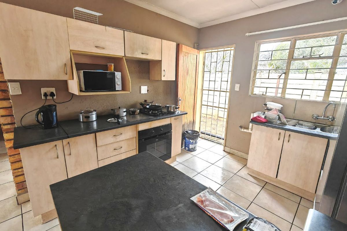 A functional kitchen featuring light wood-tone cabinetry, dark countertops, built-in oven and hob, tiled flooring, and direct access to the exterior via a security gate.