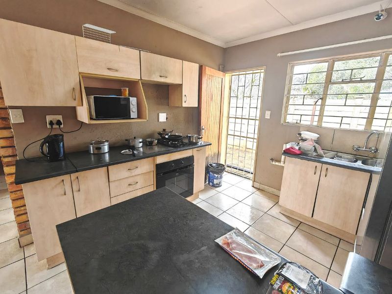 A functional kitchen featuring light wood-tone cabinetry, dark countertops, built-in oven and hob, tiled flooring, and direct access to the exterior via a security gate.