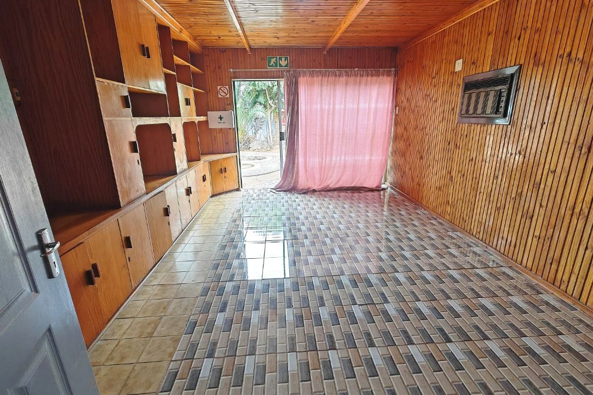 An empty living area featuring extensive built-in wooden cabinetry, timber-clad walls and ceiling, tiled flooring, and a sliding door leading to the exterior.