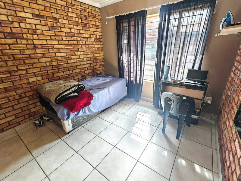 A bedroom featuring an exposed brick wall, ceramic tiled flooring, and natural light through the window.