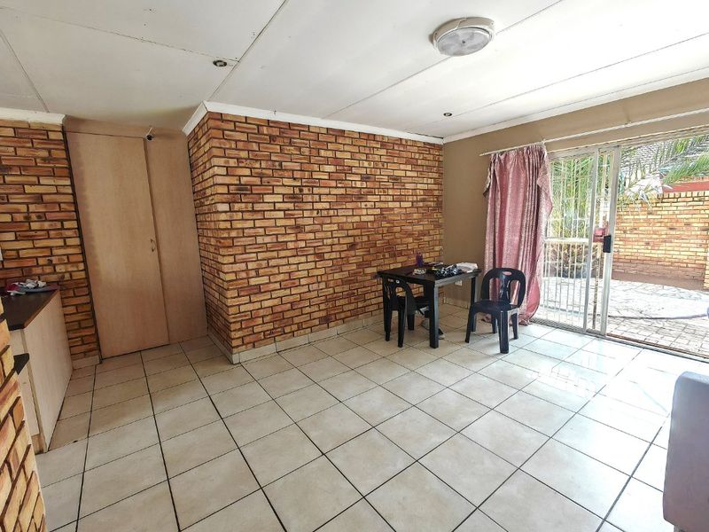 Open plan living area featuring exposed brick walls, tiled flooring, and a sliding glass door providing access to the outdoor patio area.
