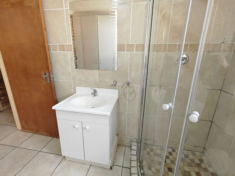 A functional bathroom featuring a corner shower enclosure, vanity cabinet with basin, and neutral wall tiling.