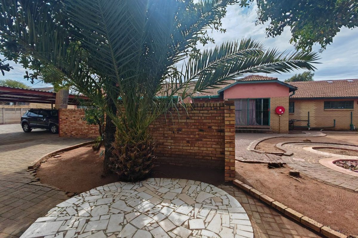 A spacious rear courtyard featuring brick boundary walls, paved areas, and a mature palm tree, providing a functional outdoor space for the property.