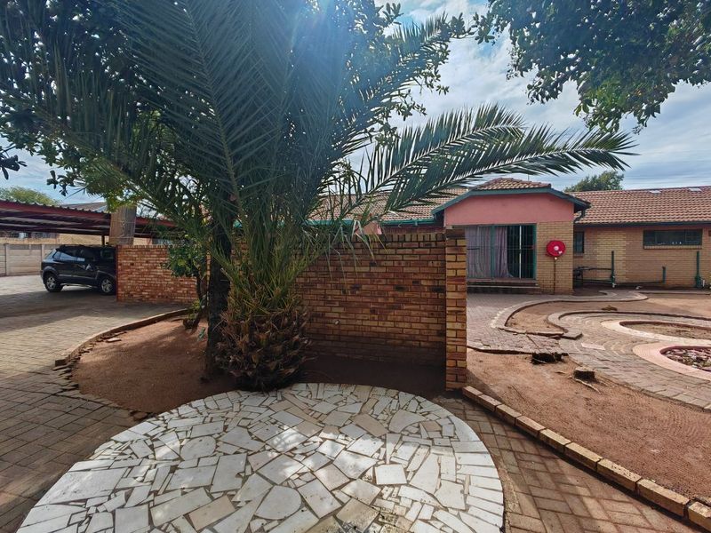 A spacious rear courtyard featuring brick boundary walls, paved areas, and a mature palm tree, providing a functional outdoor space for the property.