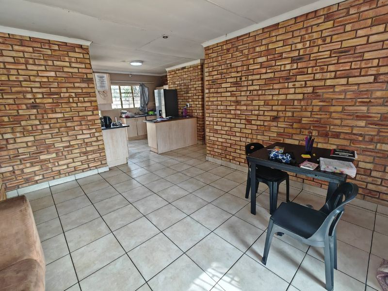 Open plan living and kitchen area featuring exposed brick walls and tiled flooring, offering a functional layout with integrated kitchen cabinetry.